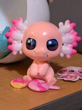 An Open "A-lot-A Axolotls"  a mini donut and sucker, sticker and the sand.